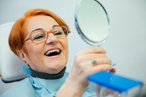 An older woman admiring her dentures while looking in a hand mirror