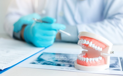 Dentist in blue gloves looking at X-ray at a desk next to set of artificial teeth