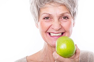 Woman with grey hair smiling holding green apple to her teeth