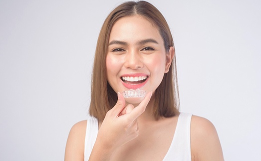 A smiling woman holding an Invisalign tray