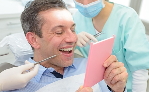 Man in dental chair looking at smile in mirror