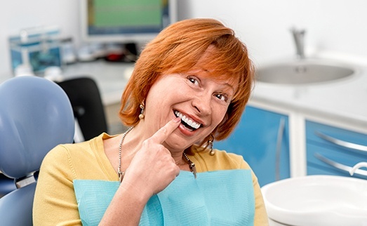 Older woman in dental chair pointing to smile